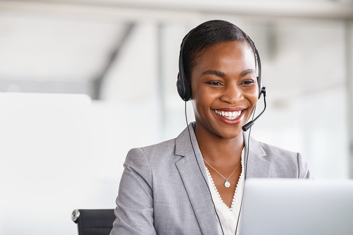 Smiling african american customer care representative working with headset in office. Beautiful black woman telemarketing agent working in call center. Call center agent with headset makinga video call with client.