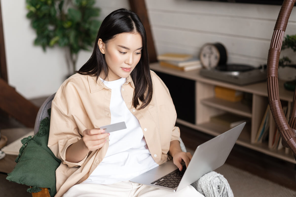 Portrait of asian young woman sitting at her home, buying on laptop, holding credit card and shopping online.