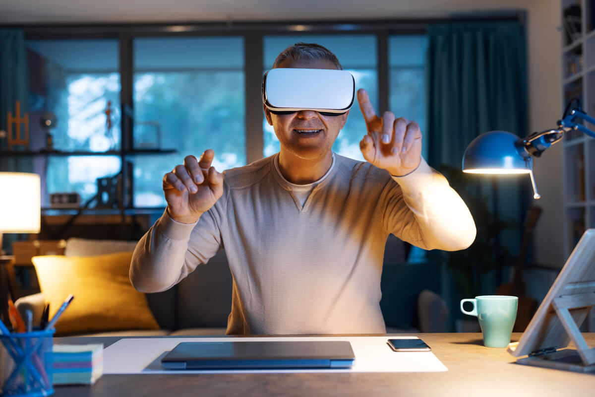 A man sitting at his desk with a VR headset is interacting with virtual screens, while smiling.